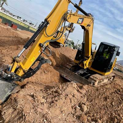 A yellow excavator digging in a construction site with a clear sky in the background.