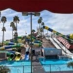 Water park with multiple colorful slides and clear pools, surrounded by palm trees and a cloudy sky.