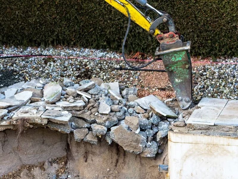 An excavator attachment breaking swimming pool concrete into rubble at a construction site in Mesa AZ.