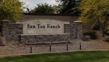 Sign for San Tan Ranch set against a stone background with trees and shrubs surrounding it.